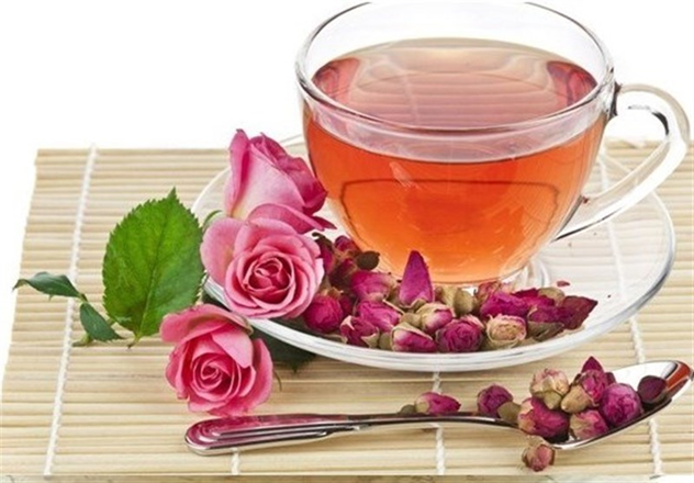 چای حاوی اسانس گل محمدی ریخته شده در فنجان شیشه ای با نعلبکی تزیین شده با غنچه های گل محمدی